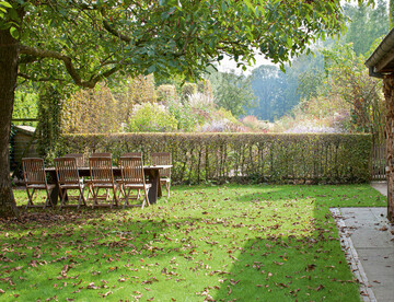 Im Frhjahr mit Zwiebelblumen berst, spendet der Walnussbaum im Sommer Schatten auf dem Rasenplatz am sdlichen Ende des Wohnhauses. ber die rahmende Hecke und die Staudenpflanzung hinweg geht der Blick in die offene Landschaft.