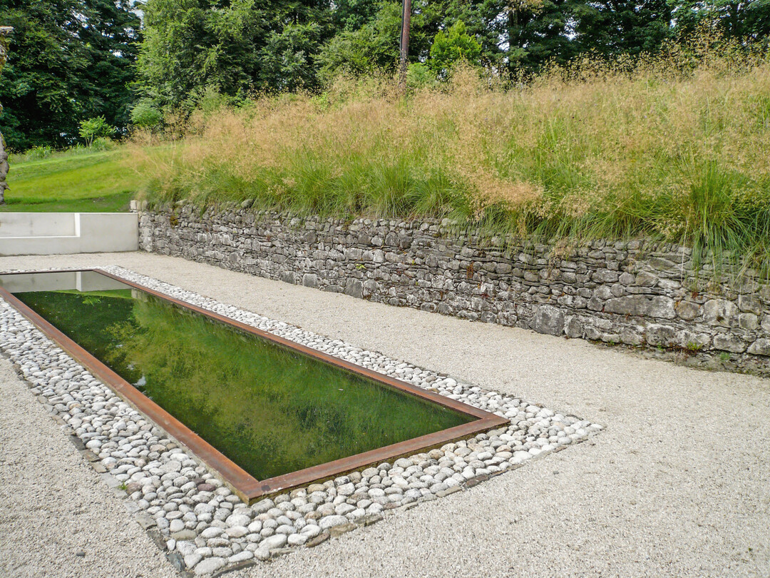 Der natrliche rostrote Farbton der Stahleinfassung des formalen Wasserbeckens schafft eine harmonische Verbindung zur Strukturvielfalt der Natursteine.