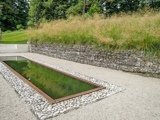 Der natrliche rostrote Farbton der Stahleinfassung des formalen Wasserbeckens schafft eine harmonische Verbindung zur Strukturvielfalt der Natursteine.