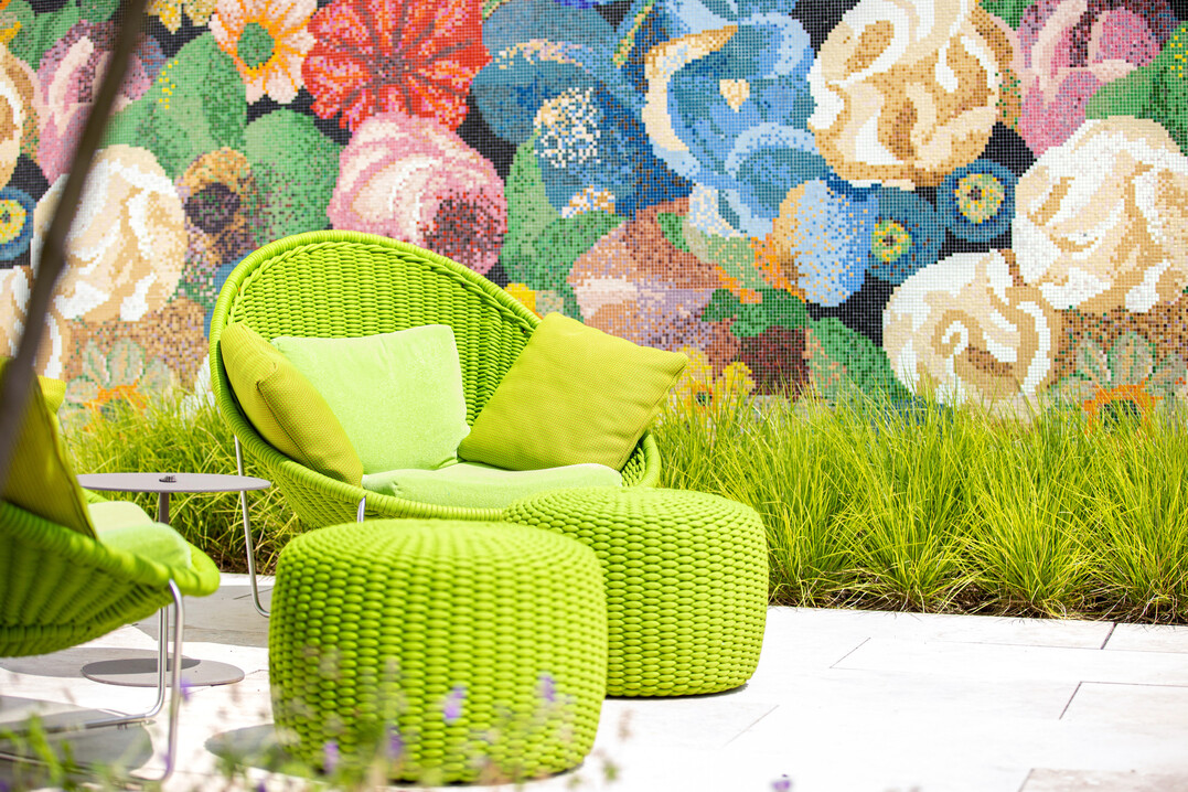 Frischgrüne Gräser verbinden das Wandmosaik aus Bisazza-Fliesen mit der farblich passenden Sitzgruppe.