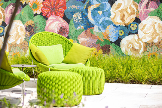 Frischgrüne Gräser verbinden das Wandmosaik aus Bisazza-Fliesen mit der farblich passenden Sitzgruppe.