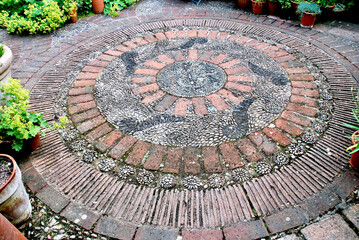 Das Ornament aus Ziegelsteinen, Ziegelriemchen sowie schmalen und breiten Kieselsteinen schmckt den Bodenbelag in einem Privatgarten in Sdengland.