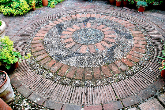 Das Ornament aus Ziegelsteinen, Ziegelriemchen sowie schmalen und breiten Kieselsteinen schmückt den Bodenbelag in einem Privatgarten in ­Südengland.