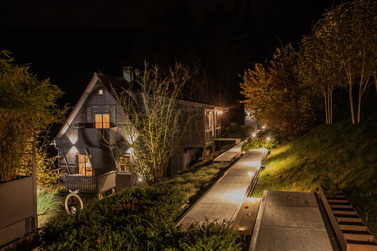 Metallstege verbinden eine moderne Villa mit einem historischen kleinen G�stehaus und einem Saunaanbau. Damit der Steg auch bei Dunkelheit angenehm und sicher zu begehen ist, wurden nur nach unten leuchtende Pollerleuchten entlang des Weges eingesetzt.