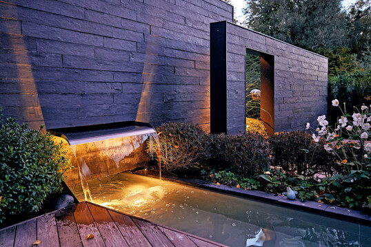 Beleuchteter Wasserfall in einem kubistisch anmutenden Garten: Harmonie in Farbe und Form