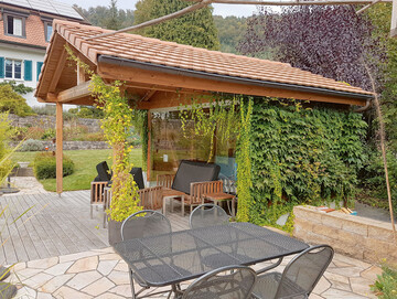 Die Baumaterialien des Pavillonswurden passend zum Bestand gewhlt und werden im Sommer von Kletterpflanzen eingenommen  diese verleihen ihm einen natrlichen Look, der optimal zum Gartenstil passt.